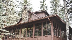 A cabin with large windows, a stone chimney, and surrounded by tall trees.