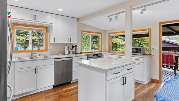 A modern kitchen with white cabinetry, a central island, and large windows offering views of greenery. - Elk Run - 2 bedroom cabin- near RMNP (Estes Park)