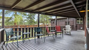 A covered outdoor deck with wooden flooring, metal railings, and various seating options including chairs and a table. - Elk Run - 2 bedroom cabin- near RMNP (Estes Park)