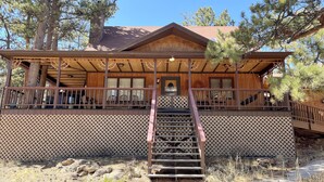 A wooden lodge with a covered porch, a staircase leading to the entrance, and a view of the surrounding trees. - Lodgepole - 2 bedroom monthly rental - Free WiFi (Estes Park)