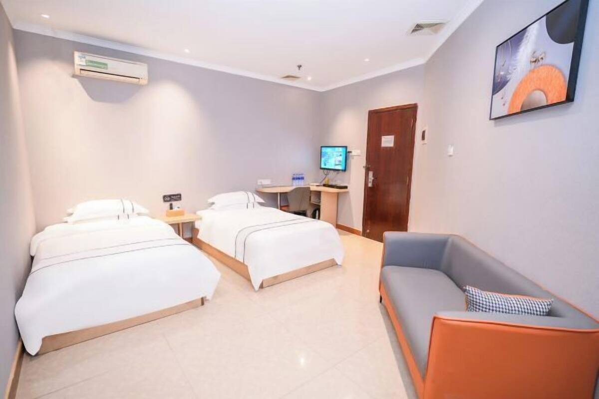 Una habitación de hotel con dos camas, un escritorio con computadora, un televisor y un sofá.