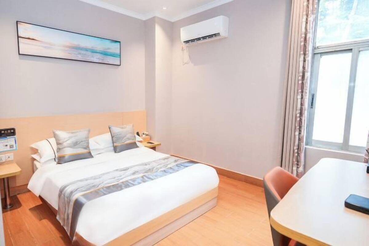 Una habitación de hotel con cama, una mesa, aire acondicionado y una ventana con cortinas.