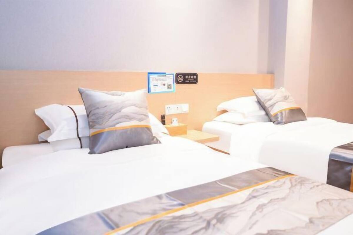 Habitación de hotel con dos camas, cada una con ropa de cama blanca y almohadas grises, cabecero de madera, mesita de noche y un cartel en la pared.