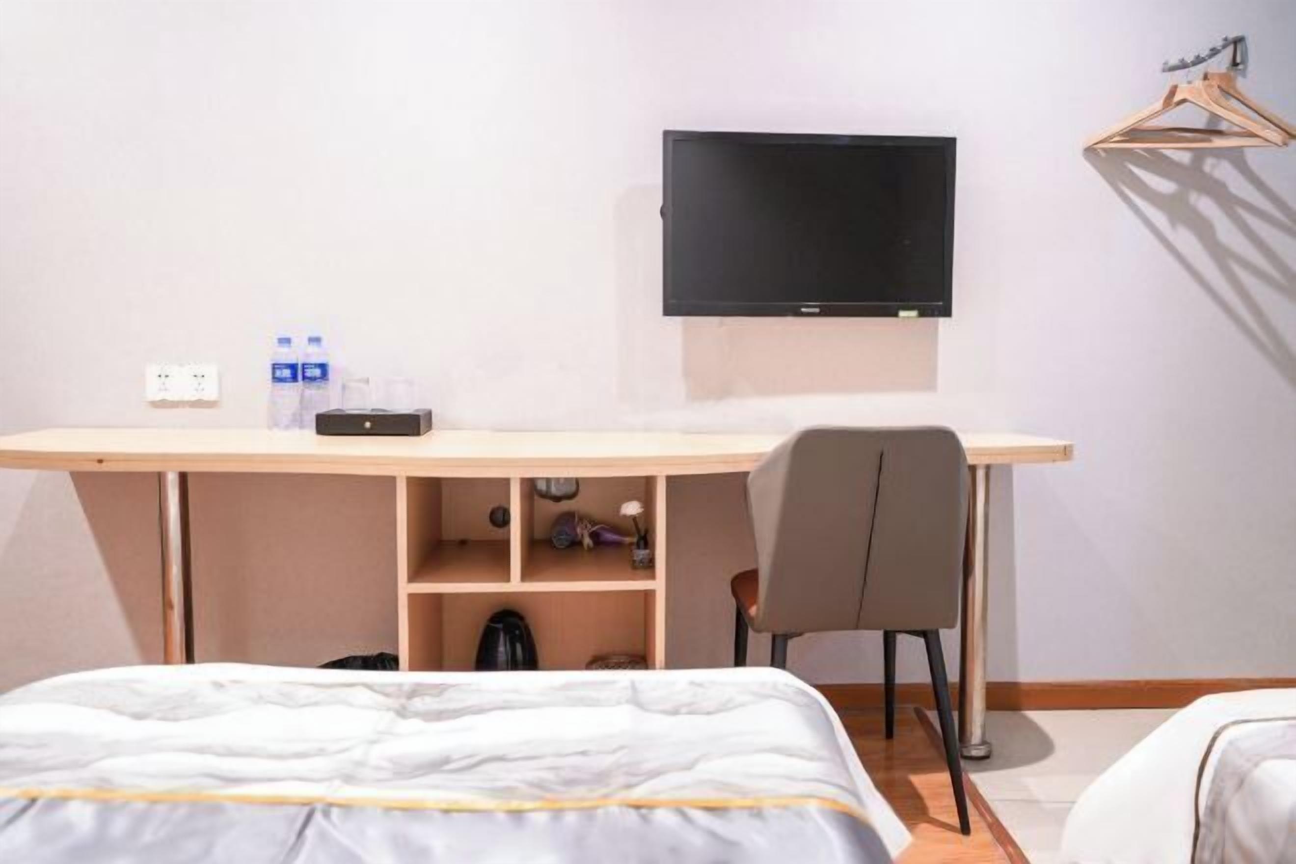 Habitación de hotel con cama, escritorio con silla, televisor montado en la pared y una botella de agua sobre el escritorio.