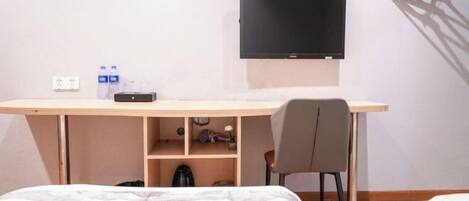 Habitación de hotel con cama, escritorio con silla, televisor montado en la pared y una botella de agua sobre el escritorio.