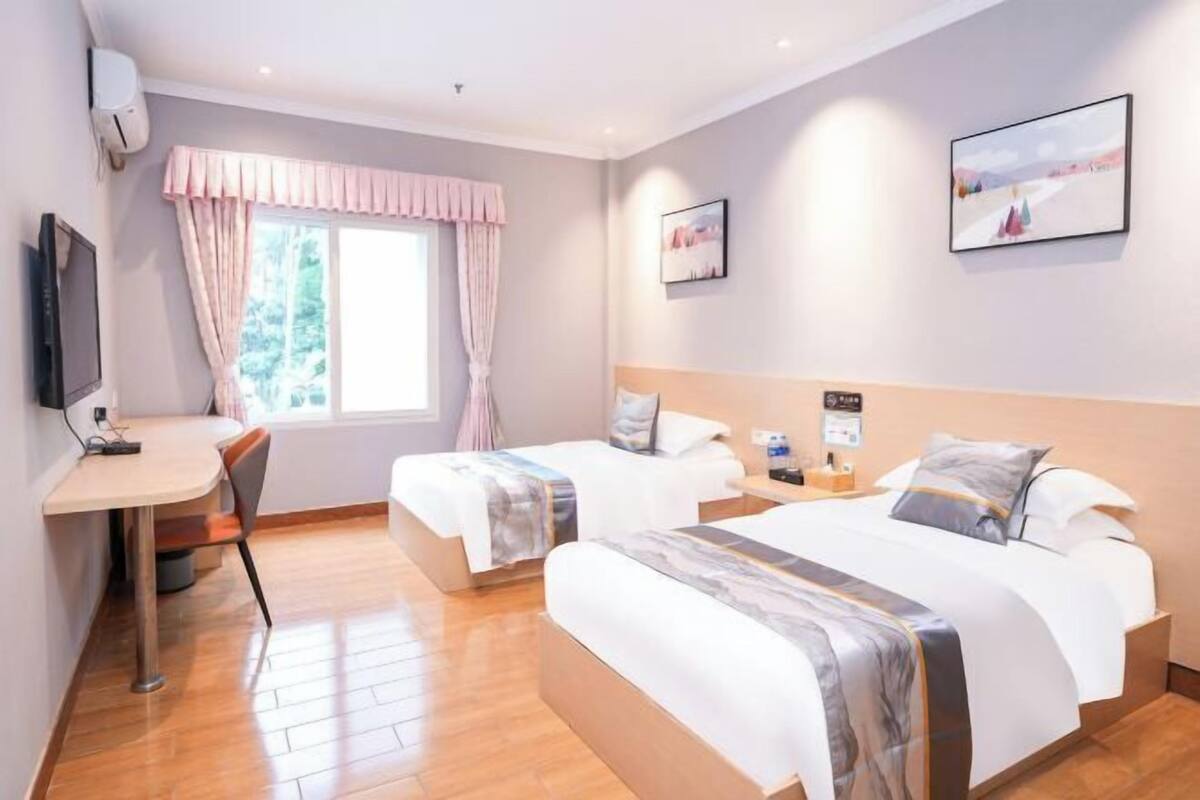 Habitación de hotel con dos camas, un escritorio, una silla, un televisor y obras de arte en las paredes.