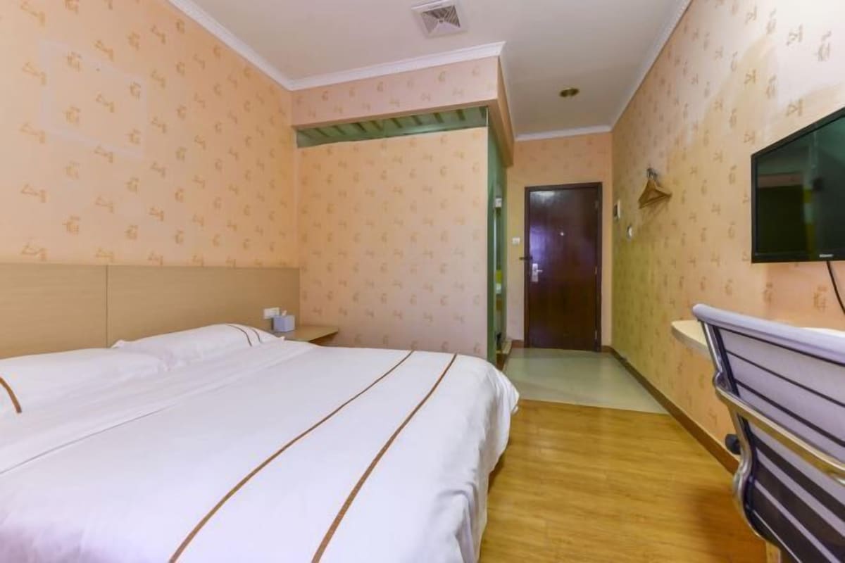 A hotel room with a bed, a bedside table, a TV mounted on the wall, and a wooden floor.