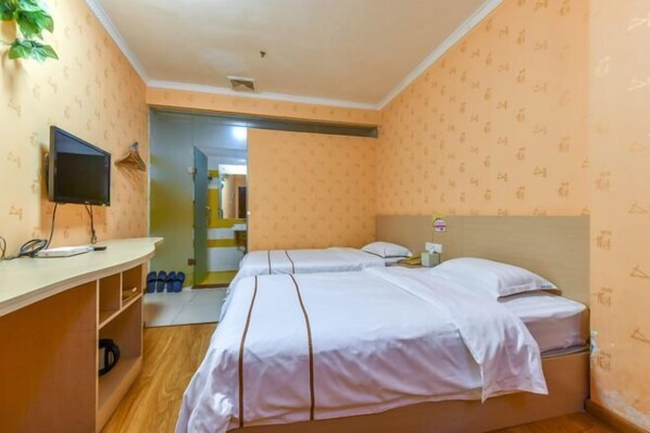 Ein Hotelzimmer mit zwei Betten, einem Fernseher, einem Schreibtisch und einem Schuhregal.