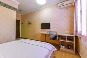 A hotel room with a bed, a desk with a chair, a TV, and a shelf with personal items. - Zhuhai Zhufeng Business Hotel (Qianshan Branch, Weinan University) (Zhuhai)