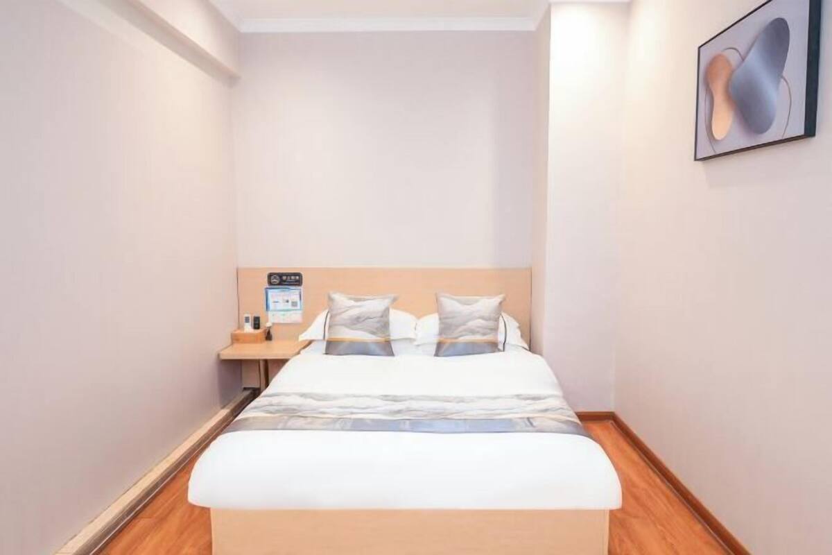 Una habitación de hotel con una cama, una mesita de noche, una obra de arte en la pared y suelo de madera.