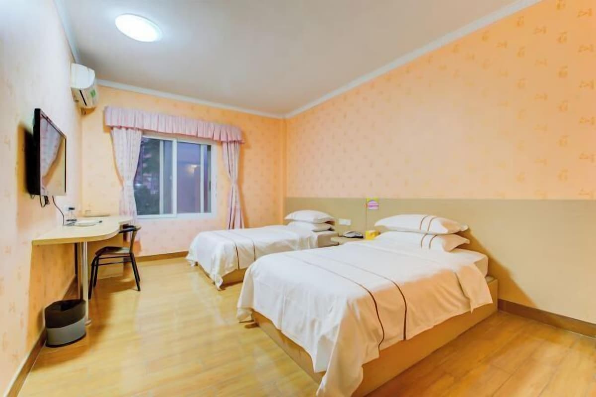 A room with two beds, a desk, a chair, and a window with curtains.
