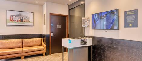 Un área de recepción con un sofá, un mostrador de recepción, un televisor montado en la pared y un cartel que dice 'Guía de Amabilidad'.