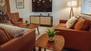 A living room with a sofa, armchair, coffee table, TV, cabinet, and lamp.