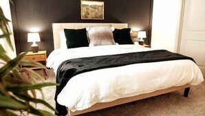 A neatly made bed with a white comforter and black throw, a wooden headboard, and two bedside lamps.