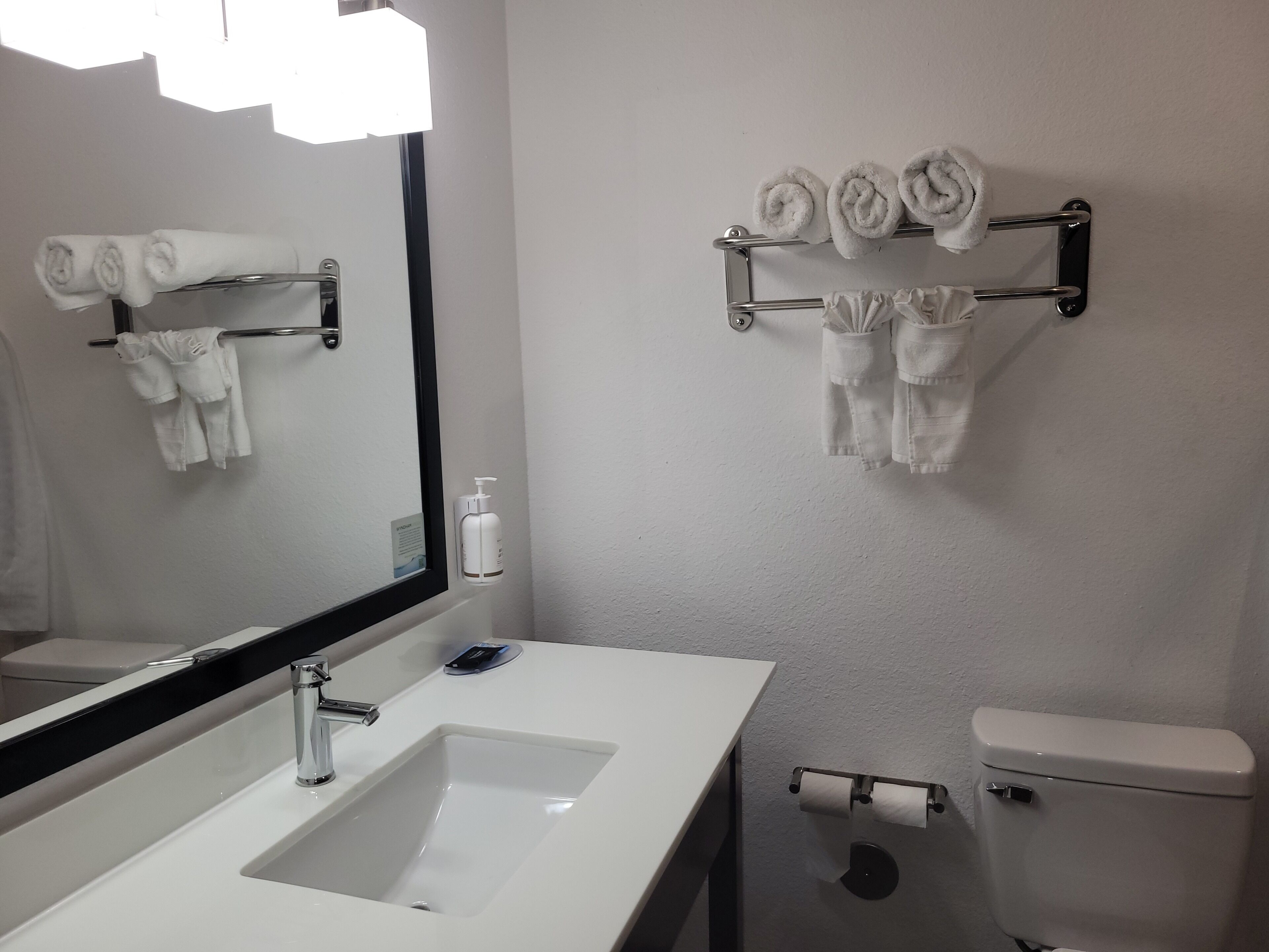 A bathroom with a sink, mirror, towel rack, toilet paper holder, and a toilet.