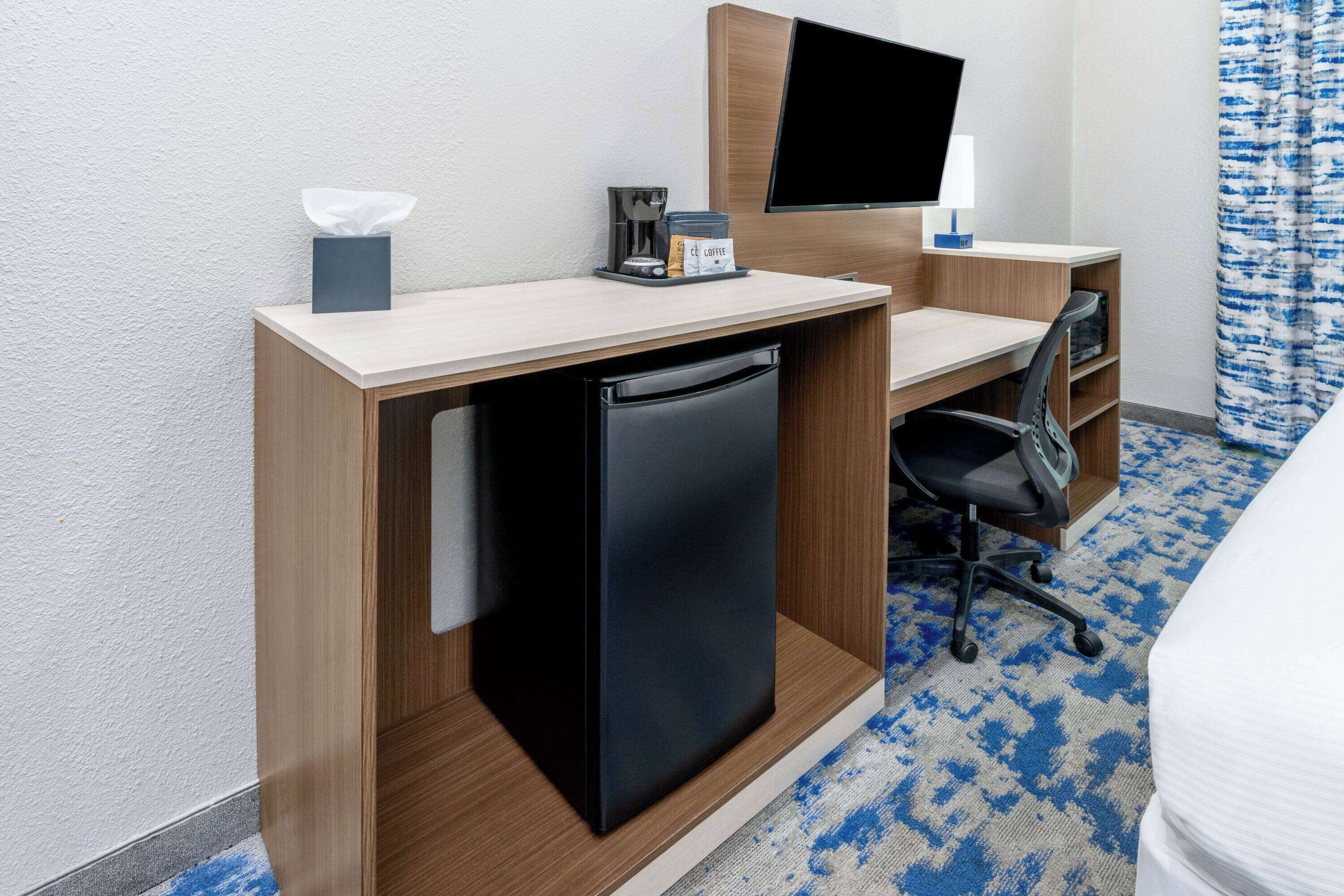 A compact hotel room with a kitchenette, a flat-screen TV, a desk, and a chair.