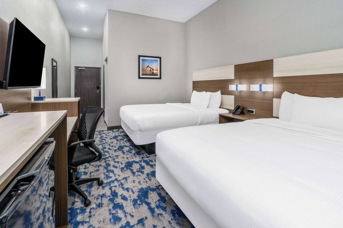 Une chambre d’hôtel avec deux lits, un bureau avec une chaise, une télévision et un tableau encadré au mur.