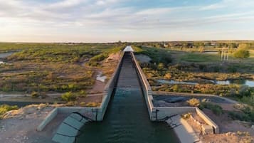 Un long barrage étroit, traversé par un cours d’eau, entouré d’un terrain aride et herbeux, où la végétation est clairsemée.