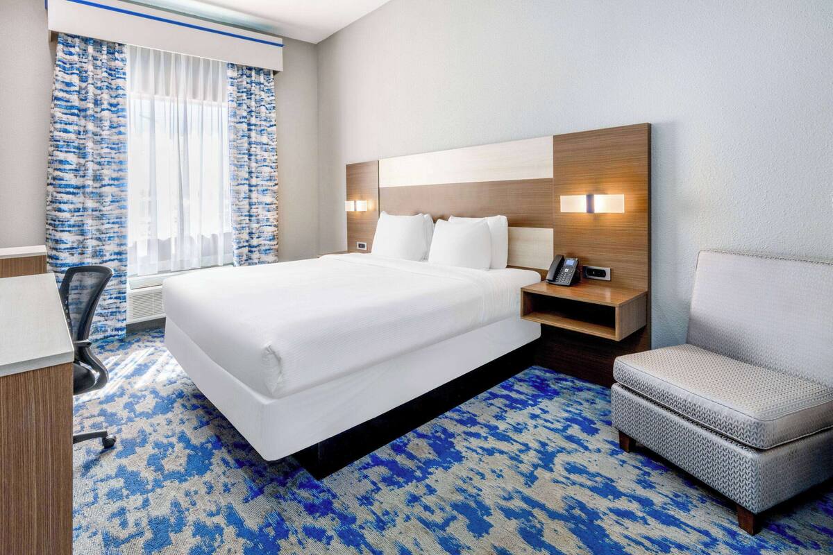 Une chambre d’hôtel avec un grand lit, une table de chevet avec un téléphone, une chaise et une moquette à motifs.