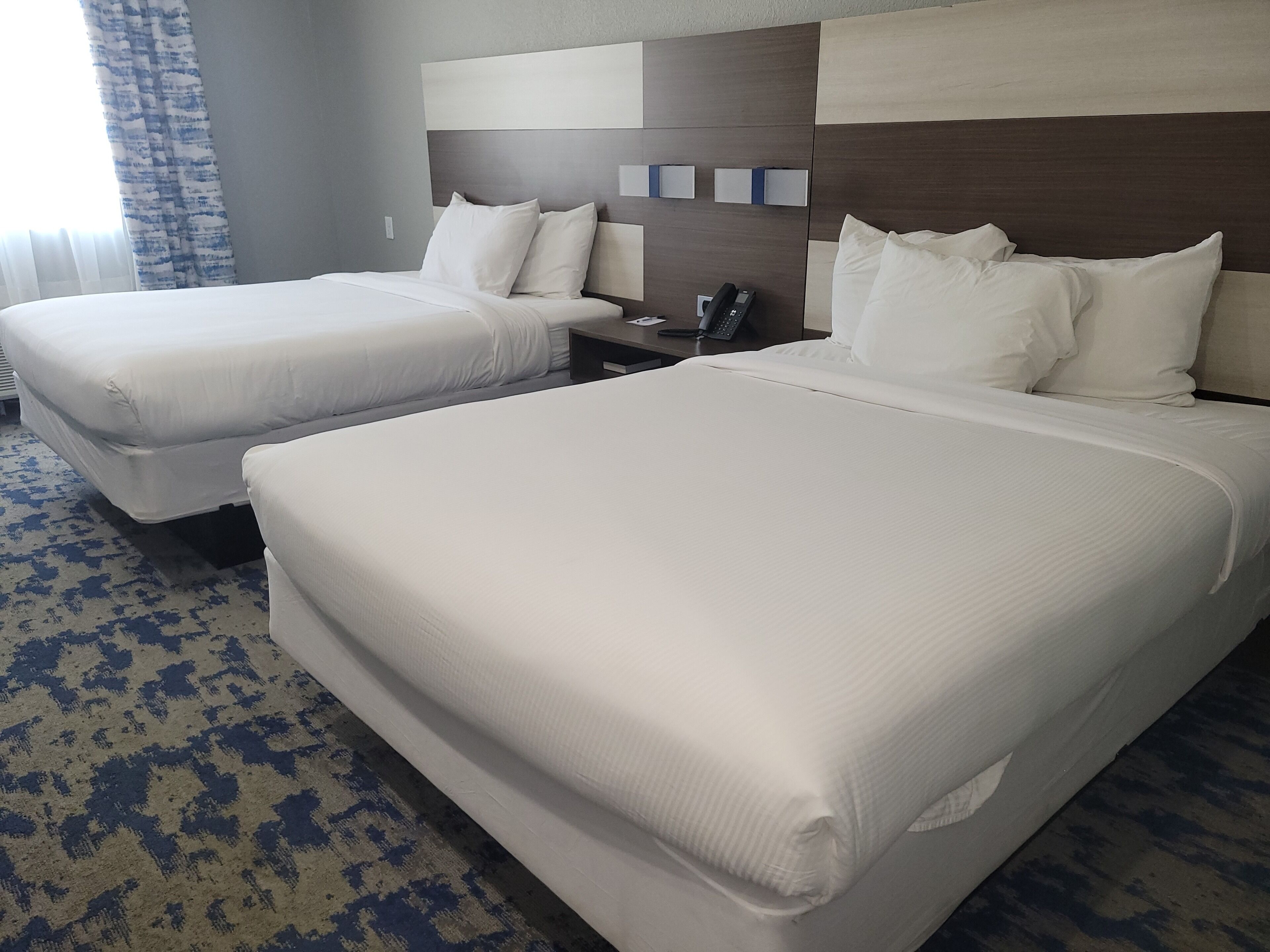 Quarto de hotel com duas camas, uma mesa de cabeceira com telefone e um tapete estampado.