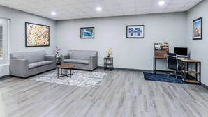 Een moderne kantoorruimte met twee grijze banken, een kleine ronde tafel, een bureau met een computer en kunstwerken in lijsten aan de muren.