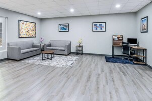 Un espacio de oficina moderno con dos sofás grises, una mesa redonda pequeña, un escritorio con una computadora y obras de arte enmarcadas en las paredes.