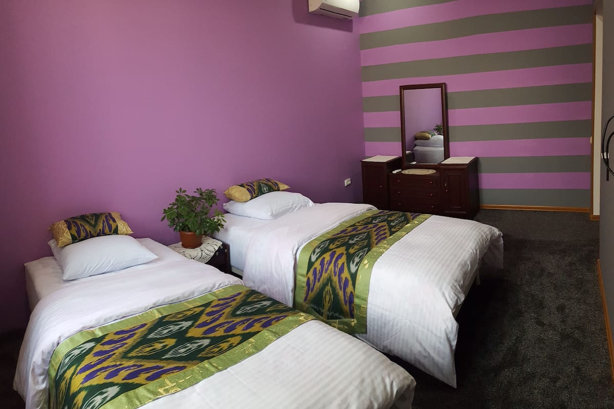 A bedroom with two beds, a potted plant, a dresser, and a mirror.