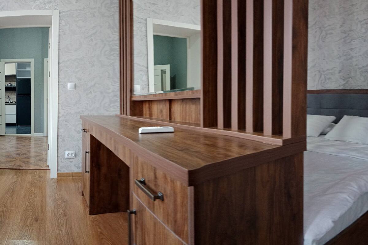 A bedroom with a wooden dresser, a bed with a grey headboard, and a nightstand.