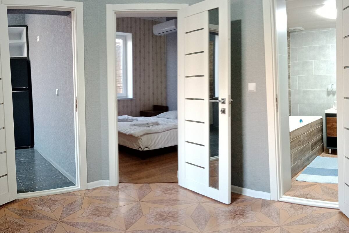 A room with a bed, a door leading to a bathroom, and a kitchen area.