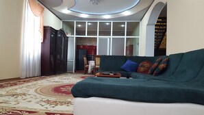A living room with a green sofa, a red and beige patterned carpet, and a large window with multiple panes. - House4you (Tashkent)