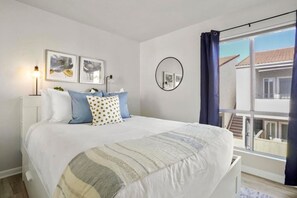 A bedroom with a bed, a bedside lamp, a window with curtains, and a balcony view.