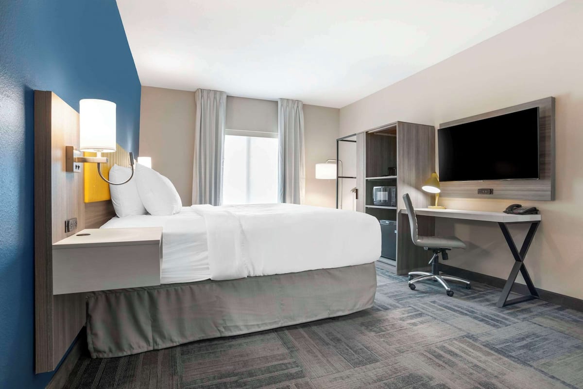 A hotel room with a bed, desk, chair, TV, and a wardrobe.