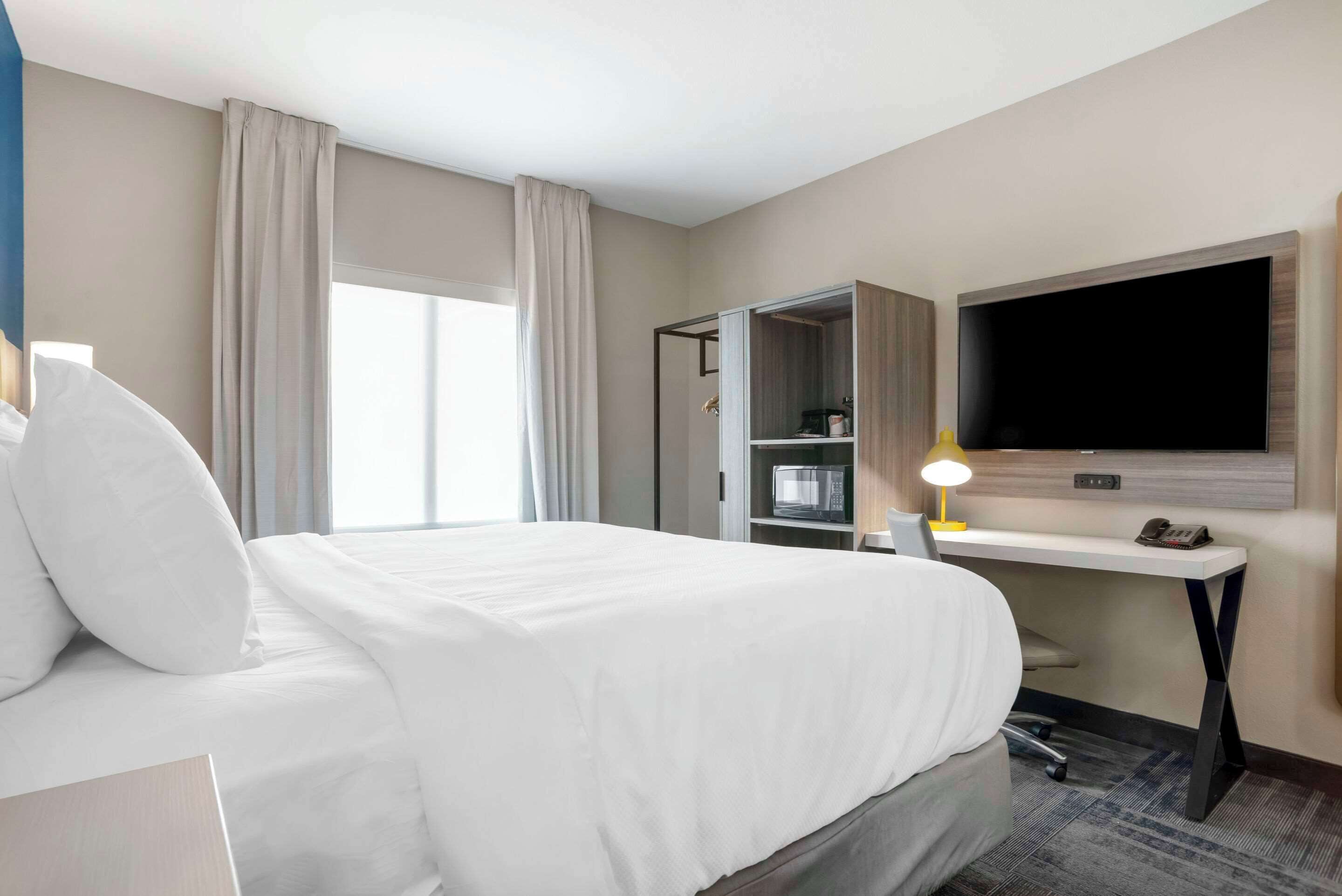 Camera d'albergo con un letto grande, una scrivania con televisione a schermo piatto, un armadio e una finestra con tende.