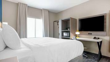 Una habitación de hotel con una cama grande, un escritorio, un televisor de pantalla plana, un armario y una ventana con cortinas.