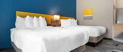 Habitación de hotel con dos camas, cabecera, mesita de noche, lámpara y una silla.