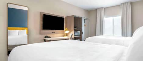 A hotel room with two beds, a desk, a flat-screen TV, and a mirror.