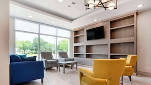 A spacious living area with a large window, a flat-screen TV mounted on a wooden wall, and a variety of seating options including a blue sofa, two armchairs, and a yellow armchair. - Comfort Inn & Suites Destin near Henderson Beach (Destin)