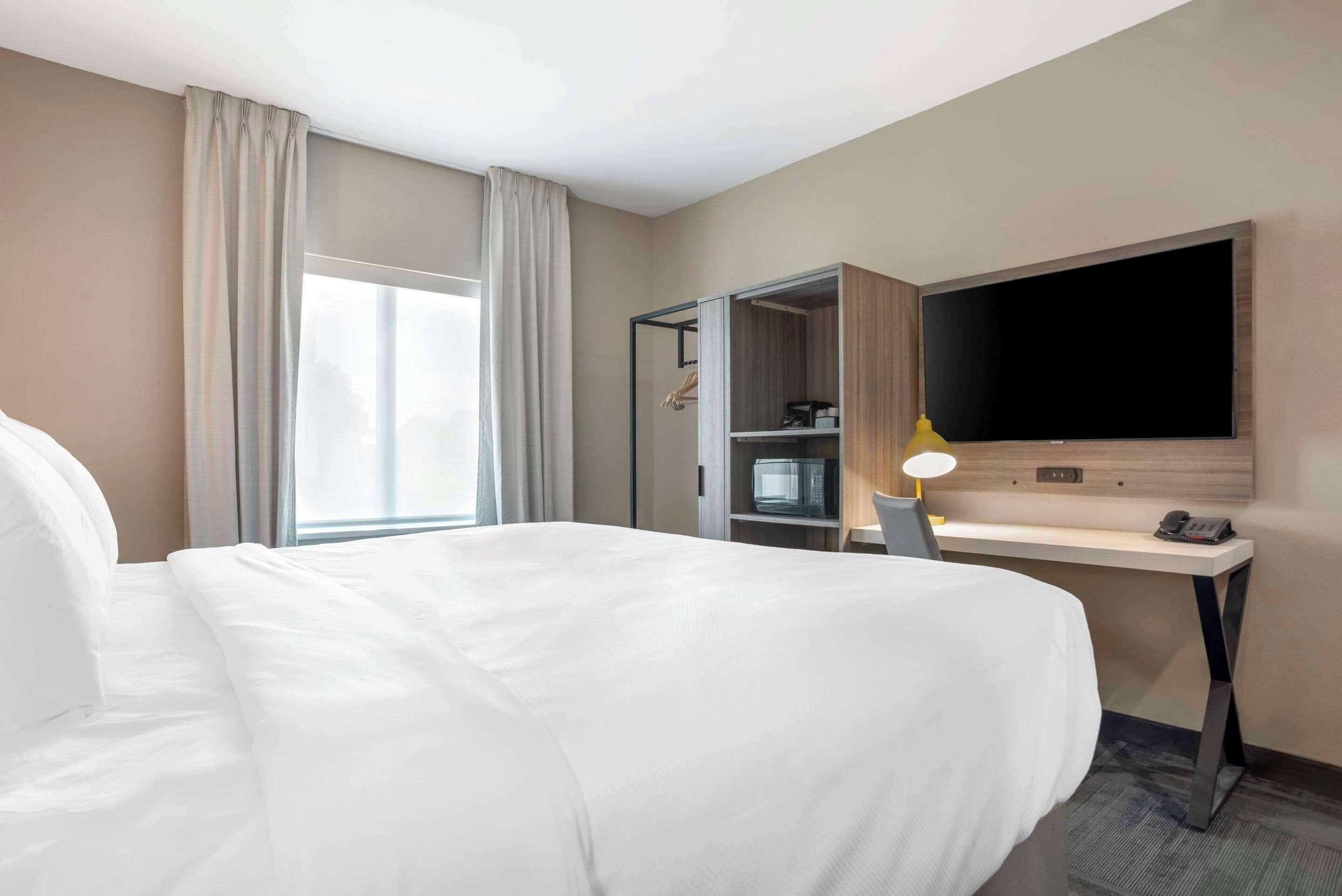 A hotel room with a large bed, a desk with a flat-screen TV, a microwave, and a wardrobe.