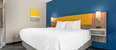 A hotel room with a large bed, a headboard with built-in lighting, a small bedside table, and a wall-mounted artwork.