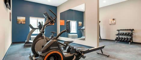 Un gimnasio con máquinas de cardio, una banca y un estante con mancuernas.