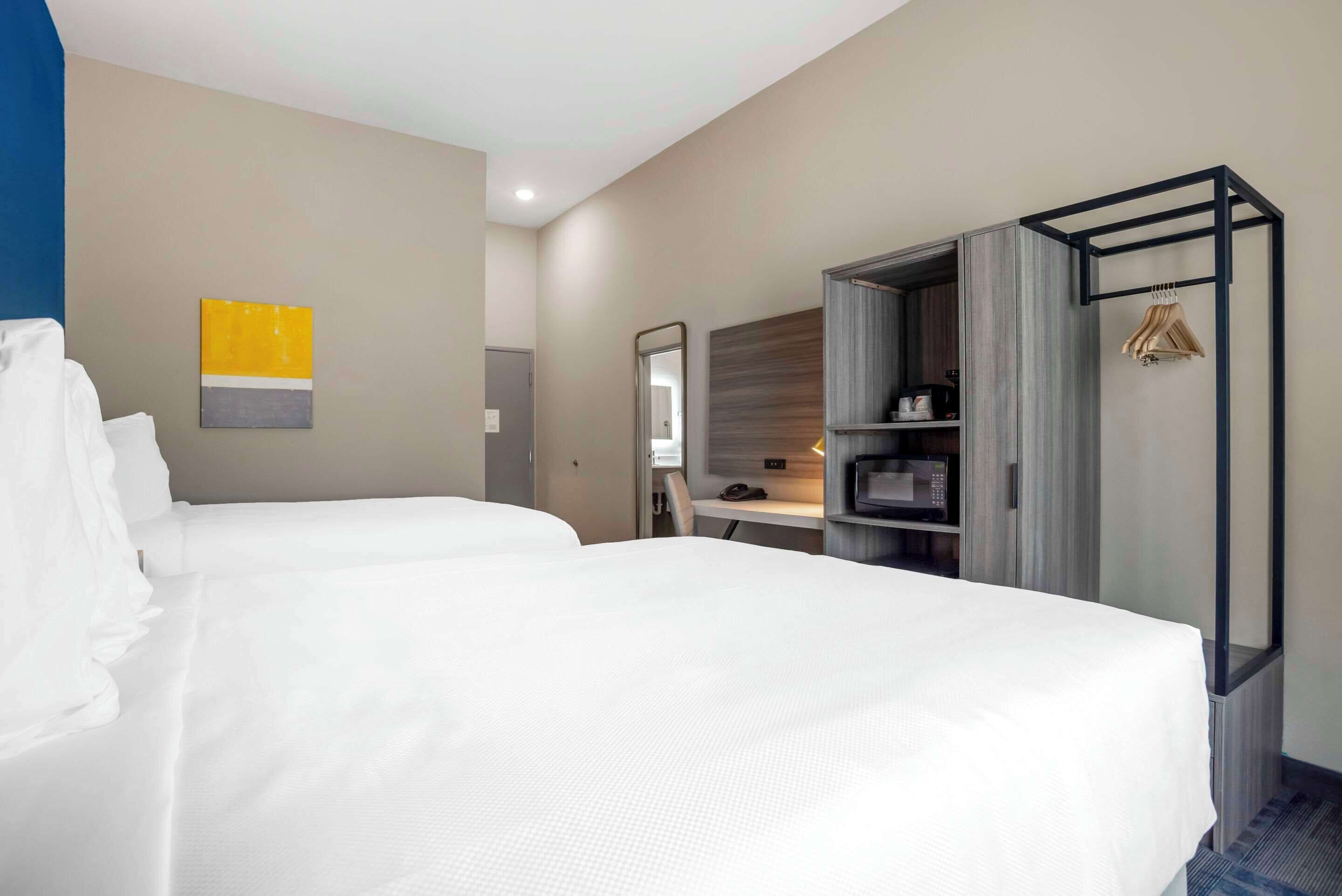 Habitación de hotel con dos camas, un escritorio con silla, armario y espejo.