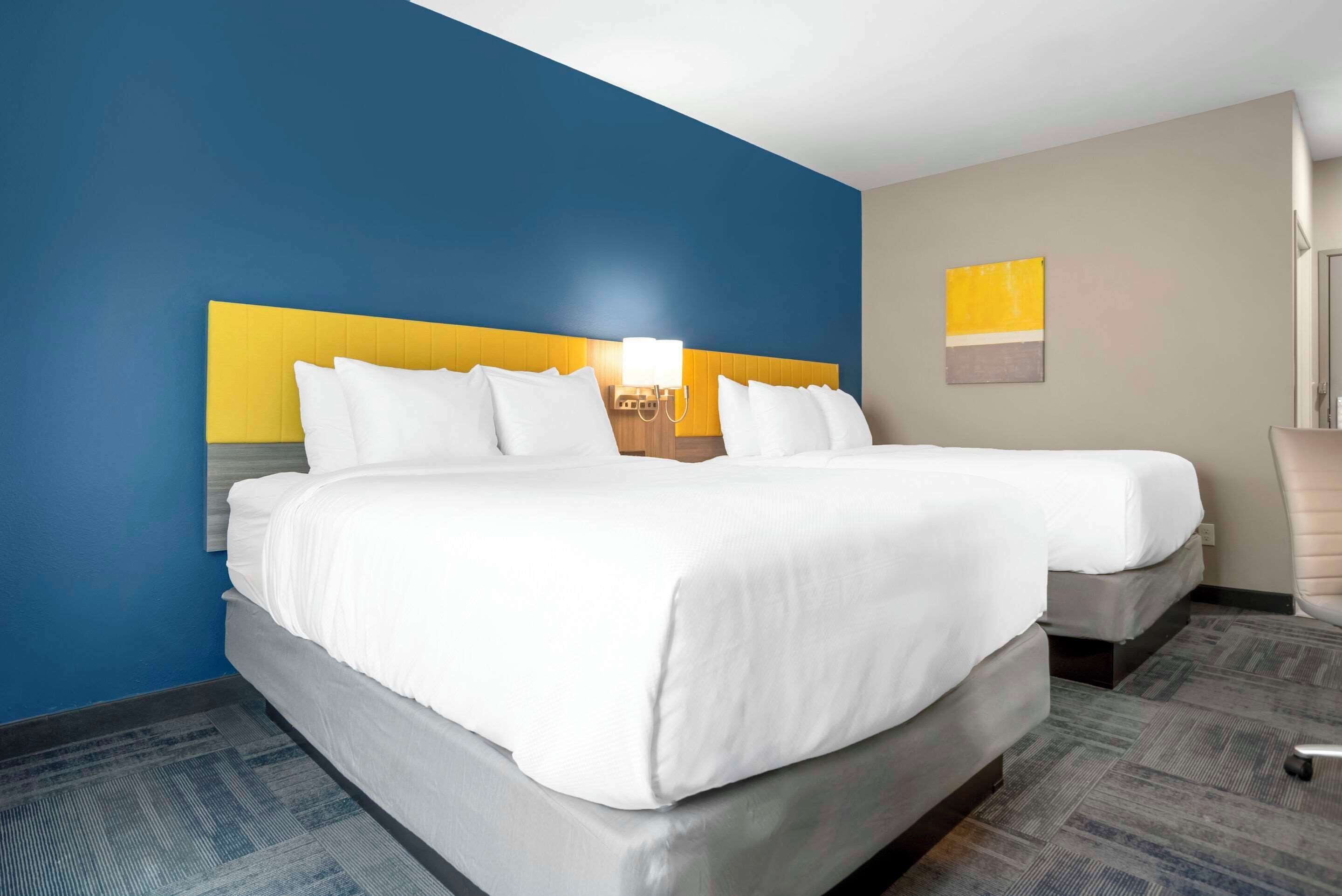 Een hotelkamer met een tweepersoonsbed, een nachtkastje met lamp en een zithoekje met een stoel.
