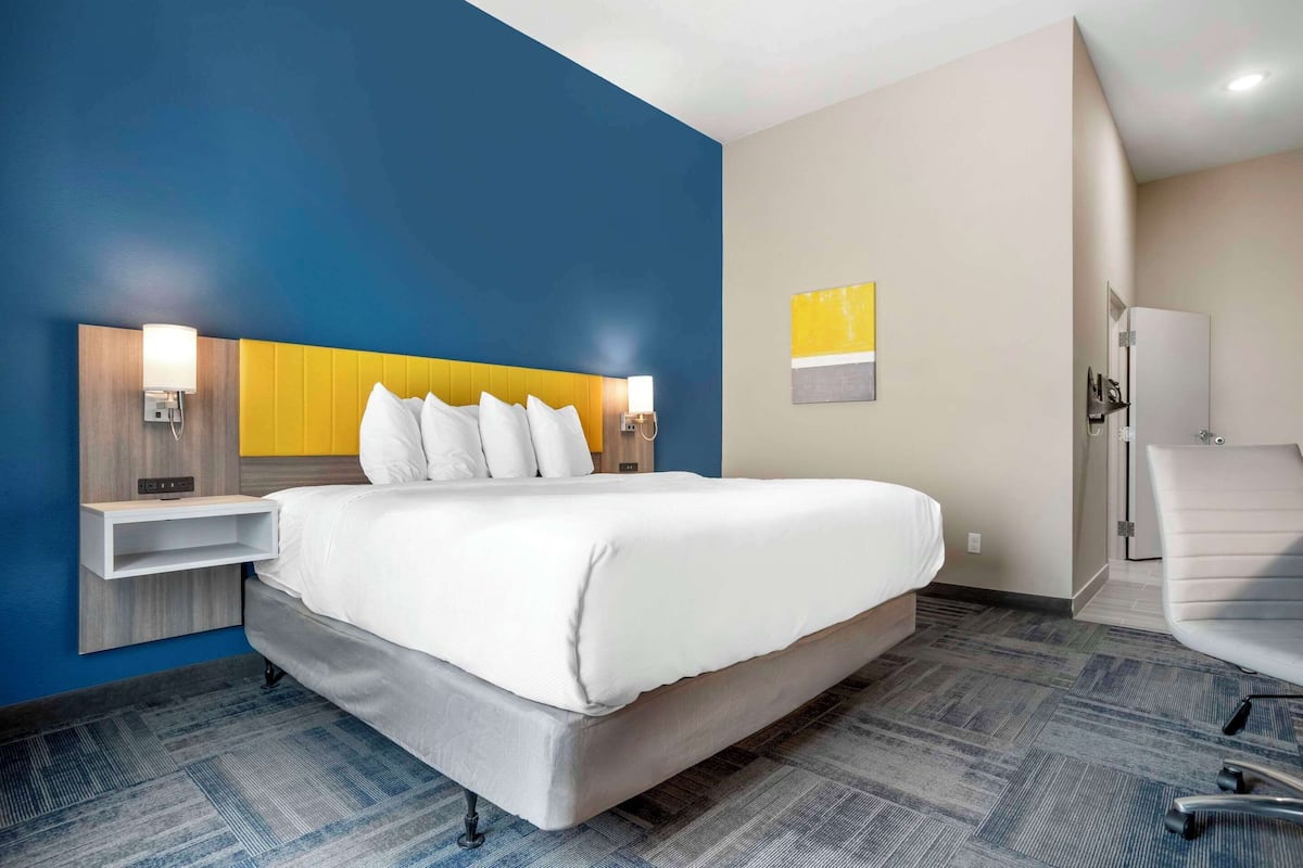 A hotel room with a bed, bedside tables, a chair, and a wall-mounted lamp.