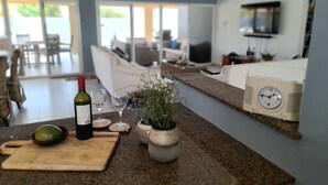 Una cucina con un piano di lavoro, una bottiglia di vino, due bicchieri, un tagliere e una pianta in vaso.