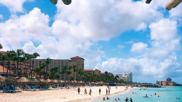 Una spiaggia con acque cristalline turchesi, palme e un albergo sullo sfondo.