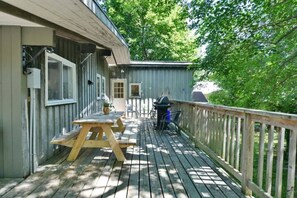 Une terrasse en bois avec une table de pique-nique et des chaises, un barbecue et un espace abrité avec une porte.