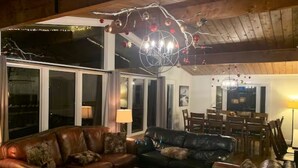 A cozy living room with leather sofas, a coffee table, and a chandelier. There is a dining area with a table and chairs. - Cozy chalet w/heated pool, hot tub, sauna 3 min dr. to the Blue Mountain village (The Blue Mountains)