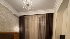 A hotel room with two beds, a chandelier, a desk with a chair, and a large window with curtains. - Solo Hotel  (Baku)