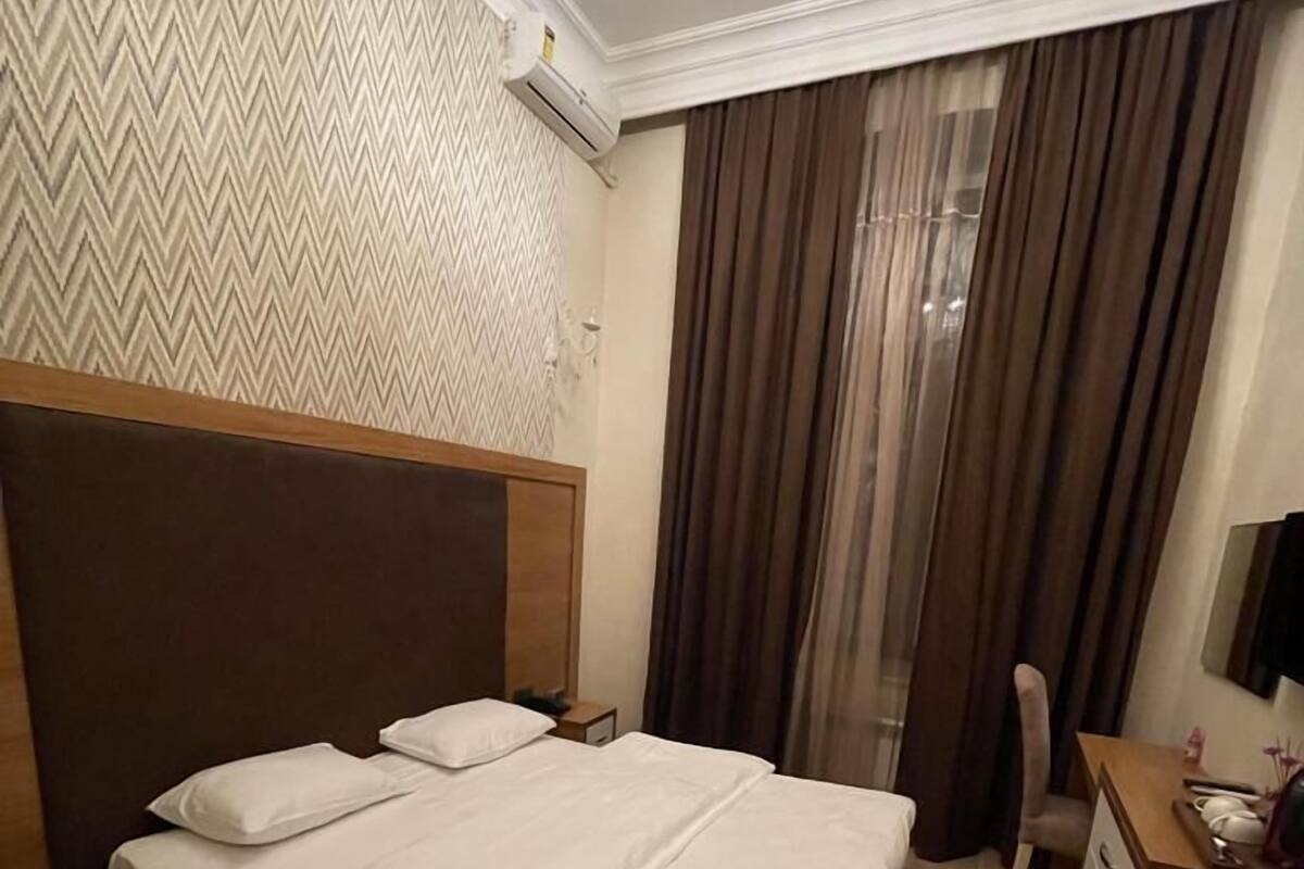 A hotel room with a large bed, a wooden headboard, a desk with a chair, a TV, and a chandelier.