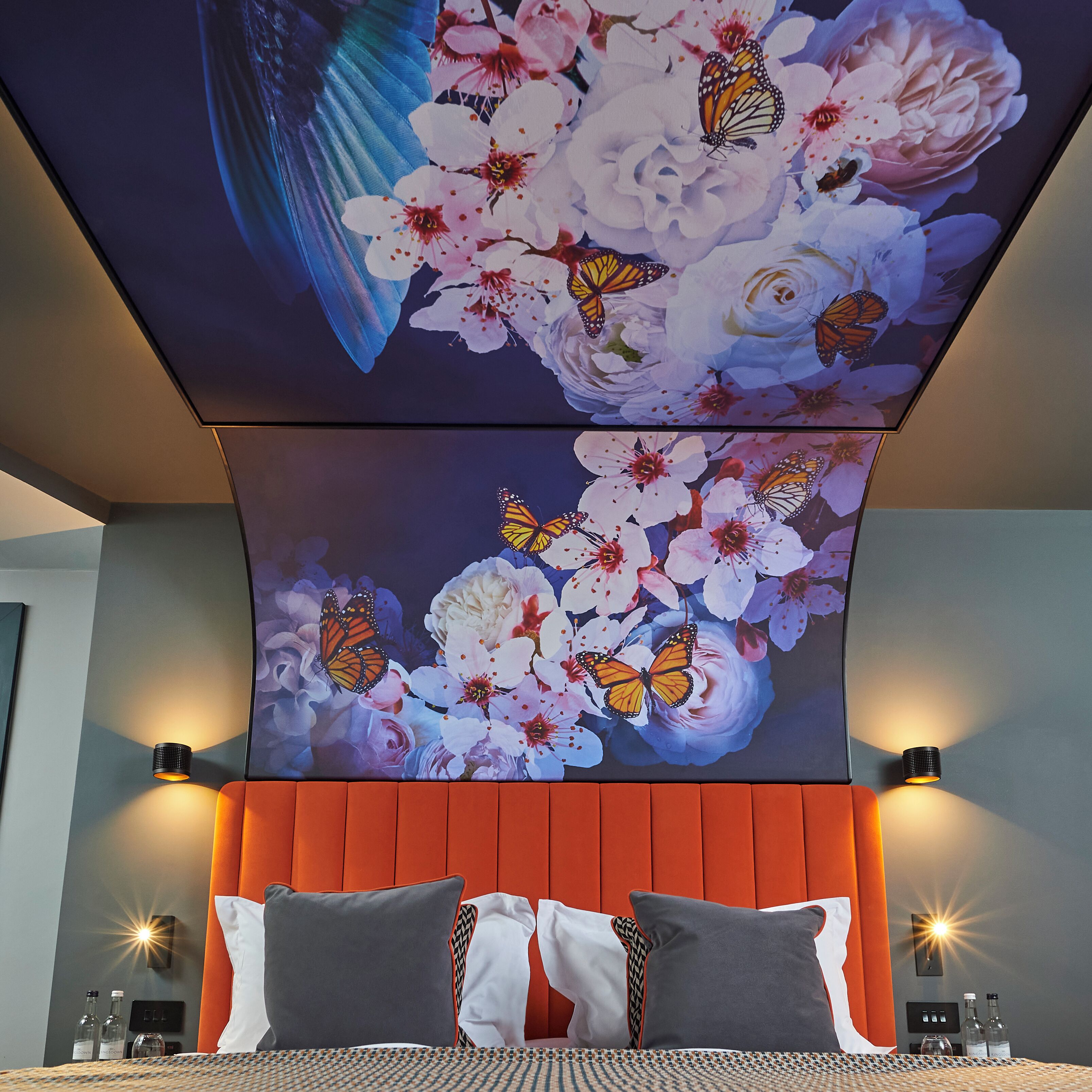 A bedroom with a large bed, two pillows, a headboard, and two wall-mounted lamps.